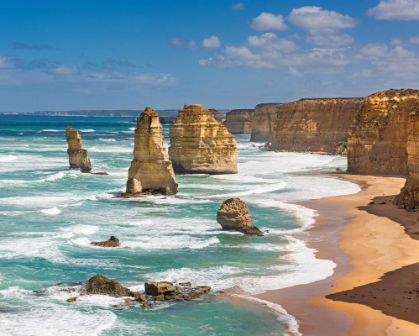 Picture of The Twelve Apostles along the Great Ocean Road in Victoria, Australia. Tall limestone stacks rise from the turquoise waters, with waves crashing against the cliffs and a sandy beach stretching along the coastline.