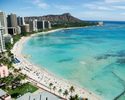 Picture of Aerial view of Waikiki Beach in Honolulu, Hawaii, featuring turquoise waters, high-rise hotels, palm trees, and the iconic Diamond Head crater in the background. The beach is lined with sunbathers and swimmers enjoying the tropical coastline.