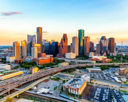 Picture of Aerial view of downtown Houston, Texas, at sunset. The skyline features a mix of modern skyscrapers and office towers, with elevated highways and busy roads weaving through the cityscape.