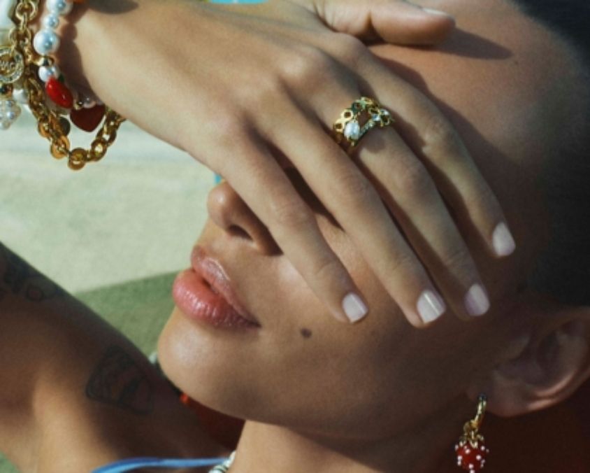 Close-up of a woman with her hand across her face, showcasing gold jewellery including rings, bracelets and earrings.