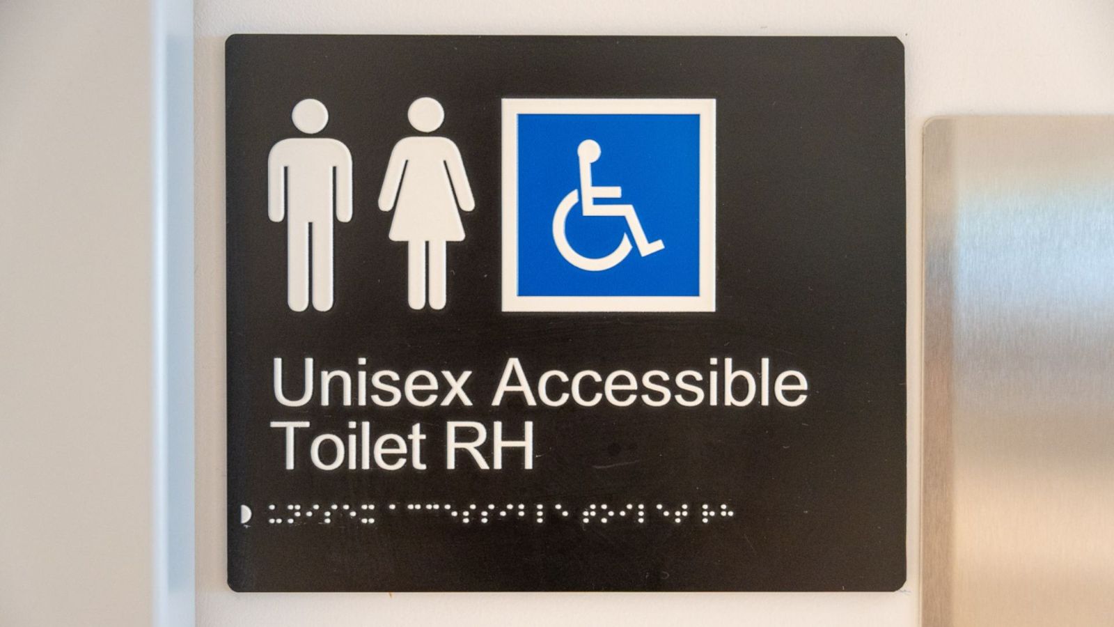 Sign indicating a Unisex Accessible Toilet. The sign features male, female, and wheelchair symbols, with braille and tactile text included.