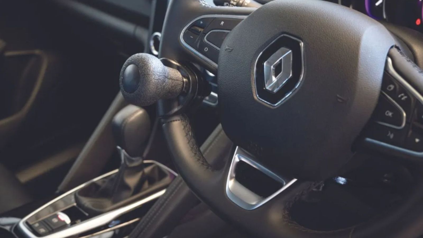Close-up of a Renault car interior showing the steering wheel with a spinner knob attachment for accessible driving, next to the gear shift and control buttons.