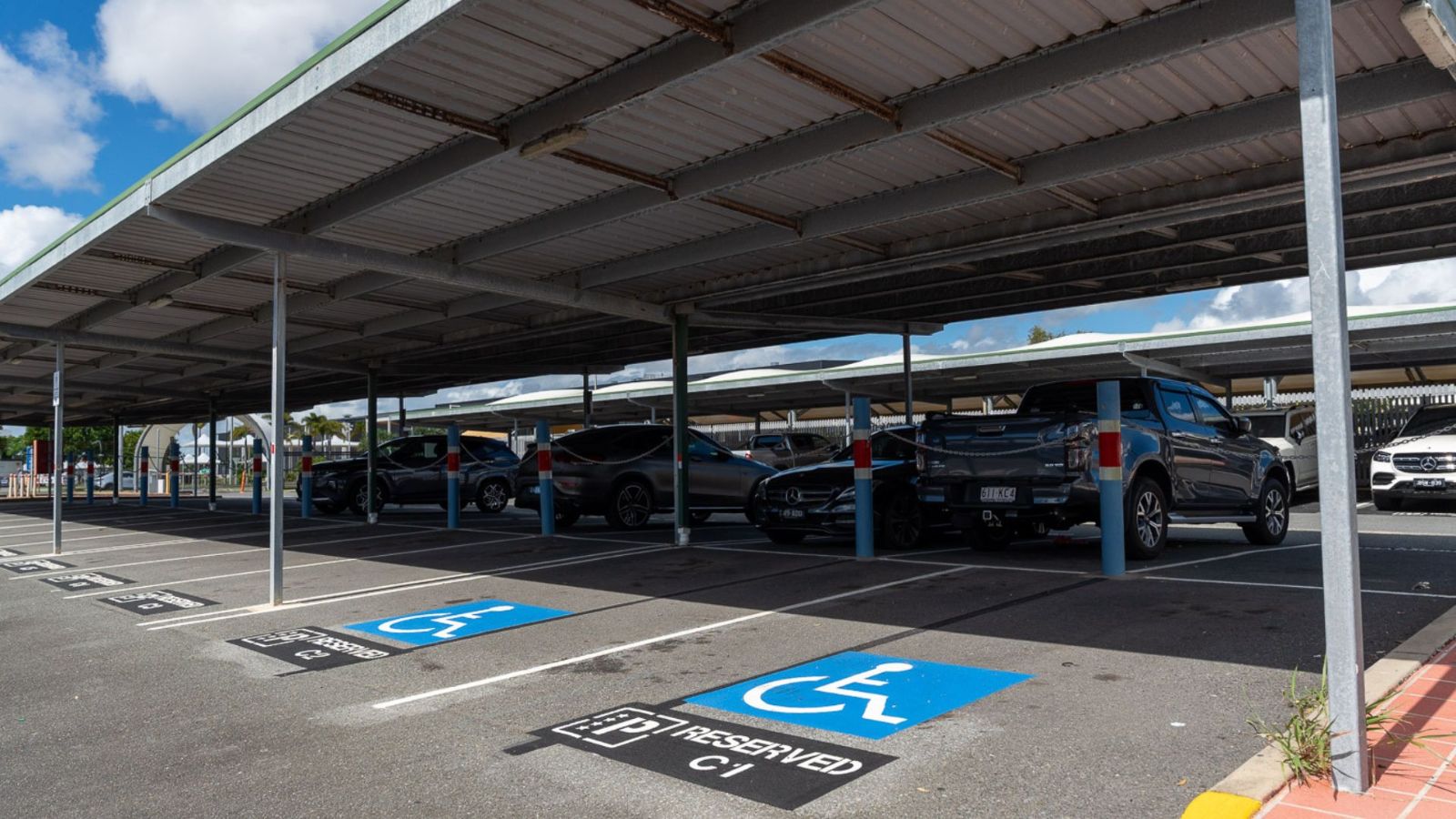 Covered airport car park with several vehicles parked, including designated accessible parking bays marked with blue wheelchair symbols and signage reading “Permit Required.”