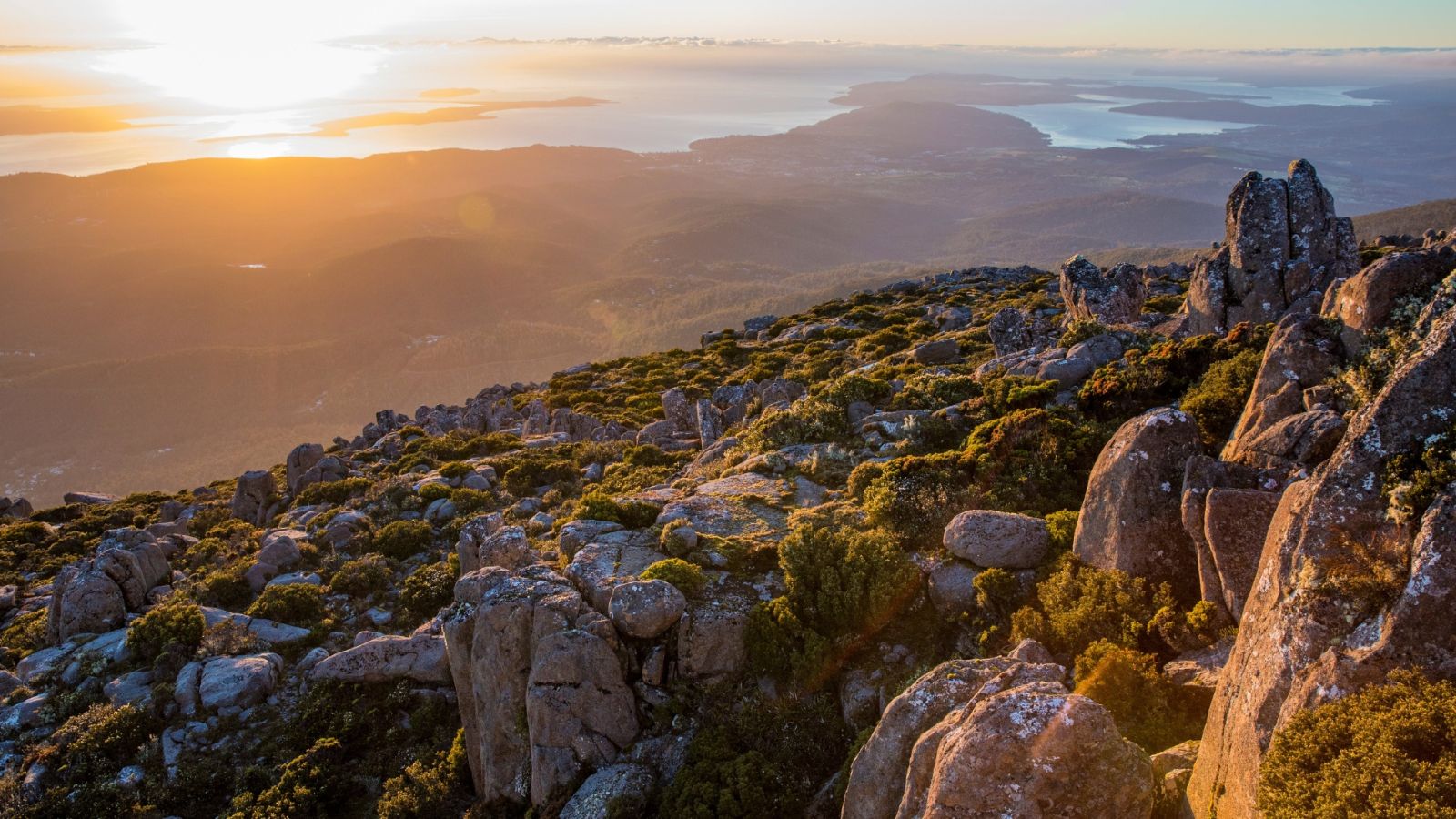 Rocky mountain landscape overlooking Hobart and surrounding waterways at sunset.