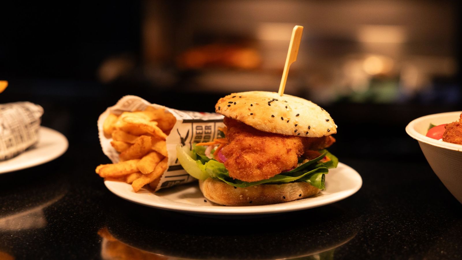Close-up of a crispy chicken schnitzel burger with lettuce and onion on a seeded bun, served with golden fries in paper wrap at Schnitz Gold Coast Airport.