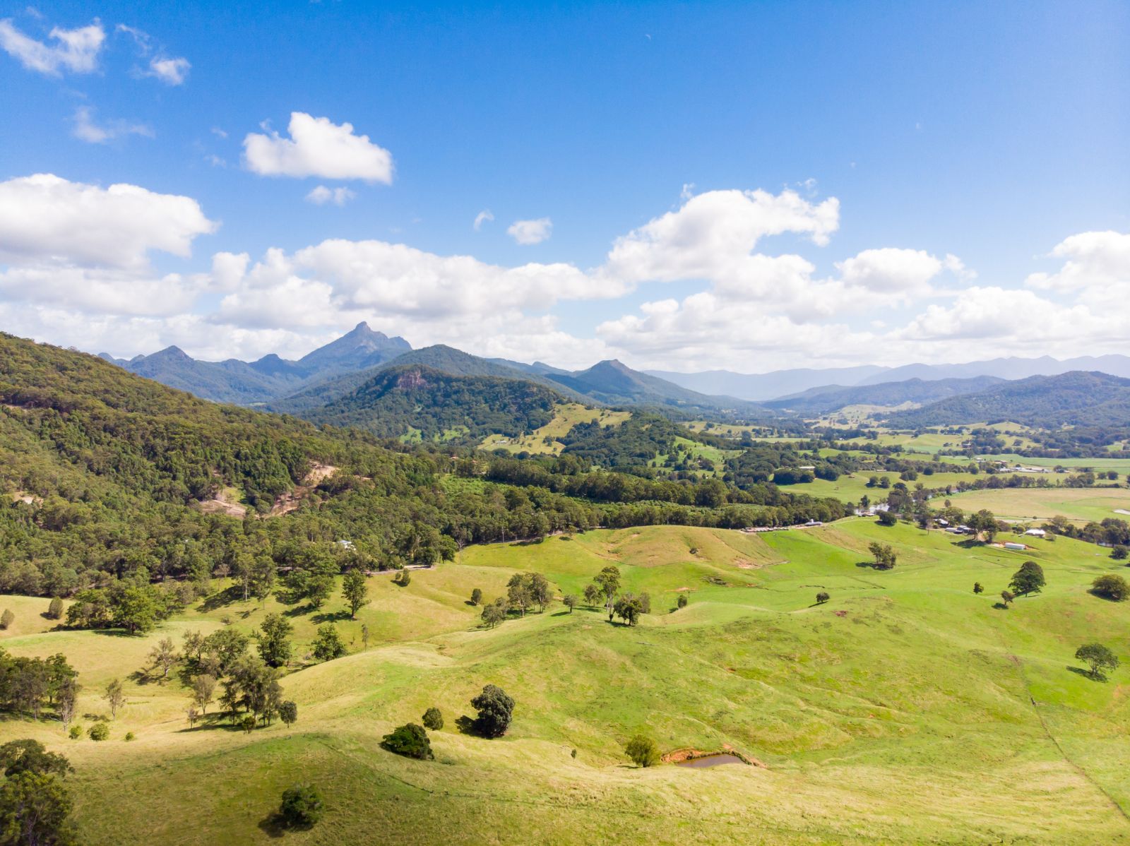 Arial view of Tweed Valley, showing long, green mountainous plains in the foreground and Mount Warning (Wollumbin) in the background.