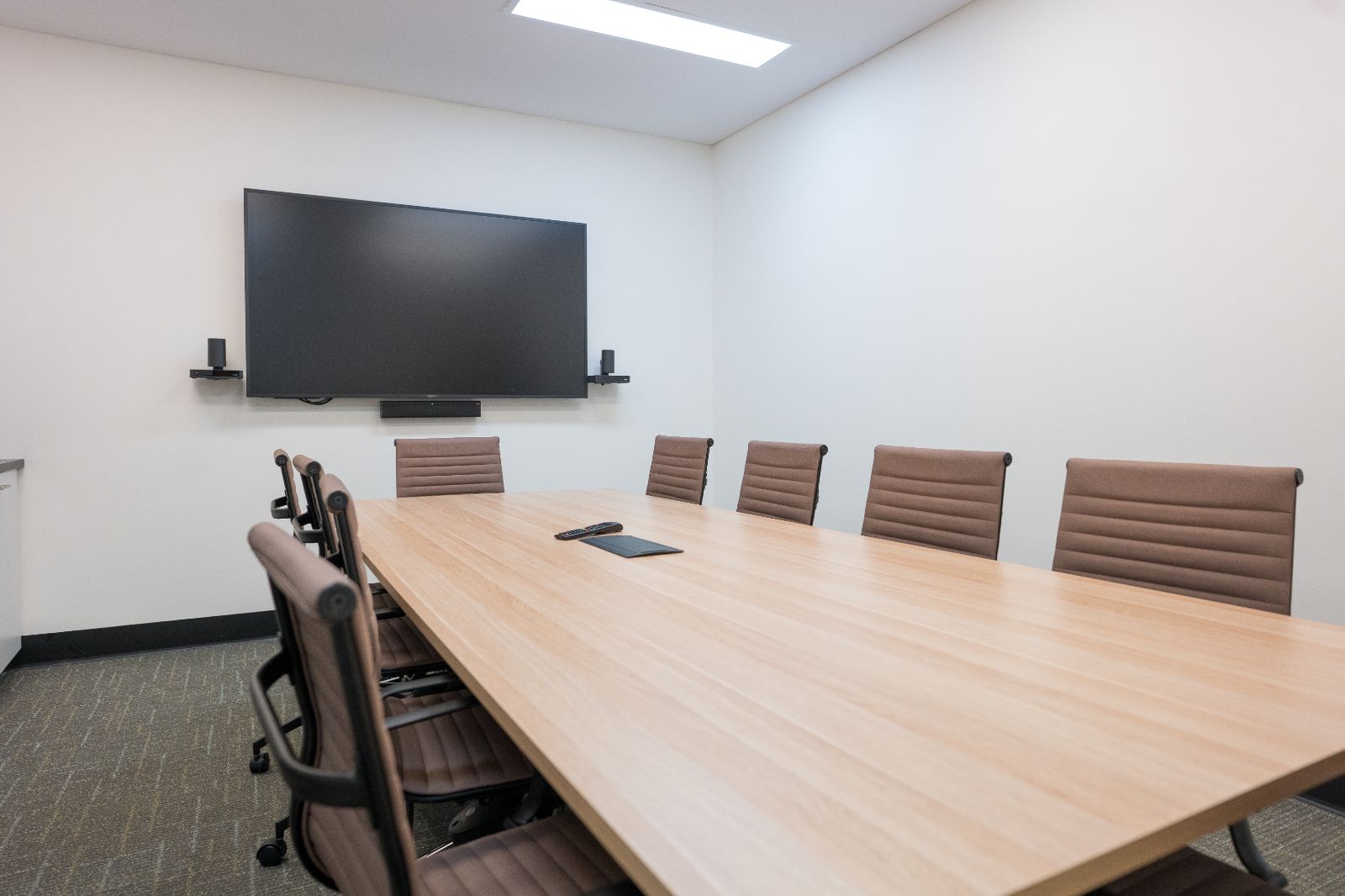 Interior of the Gold Coast Airport terminal meeting room showing a modern boardroom table with seating for up to 10 people, a wall-mounted TV screen with speakers, and a bright, neutral workspace.