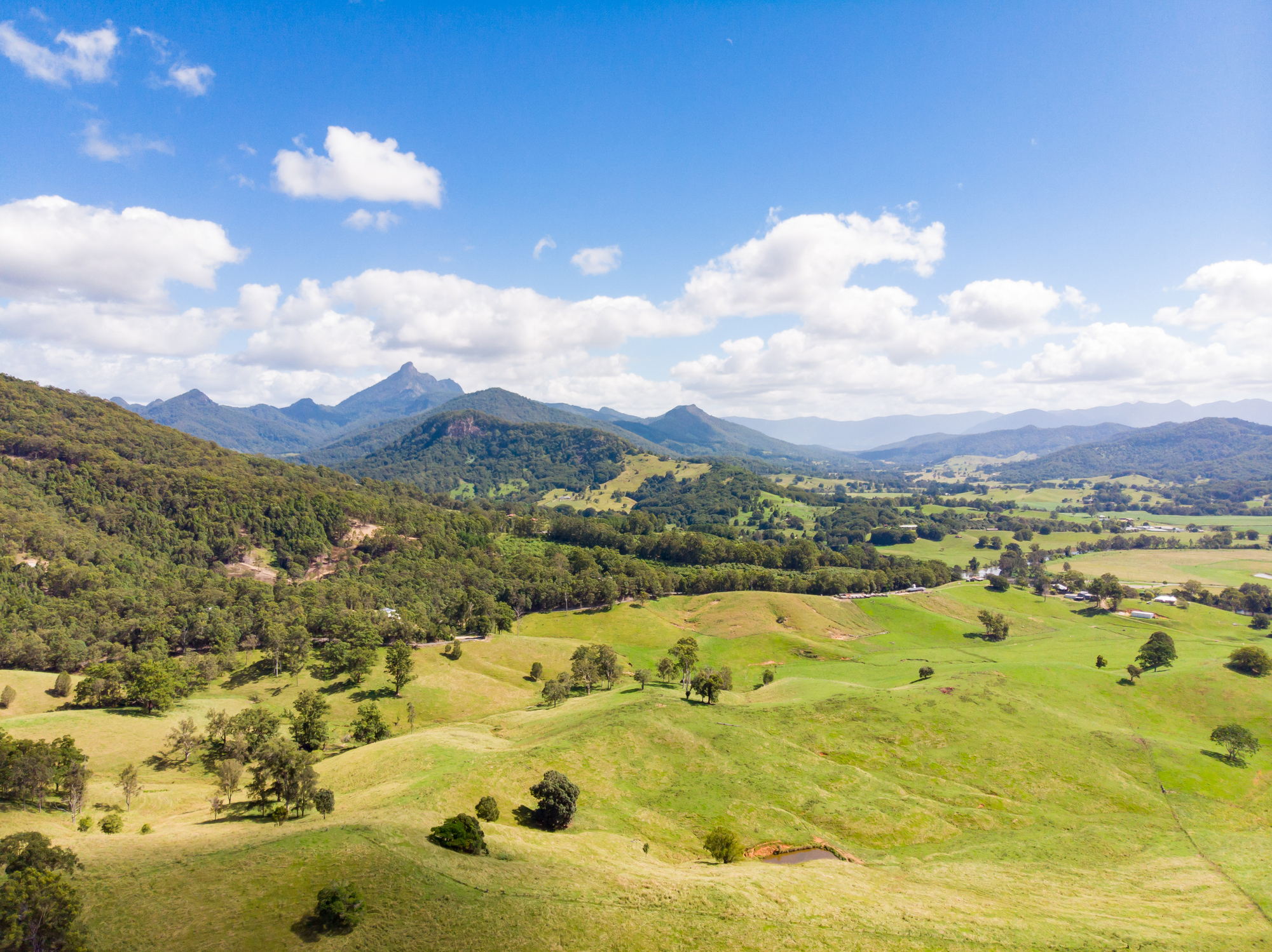 Arial view of Tweed Valley, showing long, green mountainous plains in the foreground and Mount Warning (Wollumbin) in the background. 