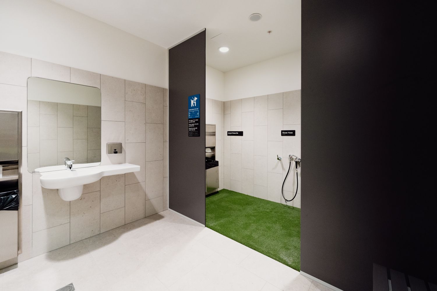 A tiled Pet Relief Area with artificial grass, a wall-mounted rinse hose and sink with mirror.